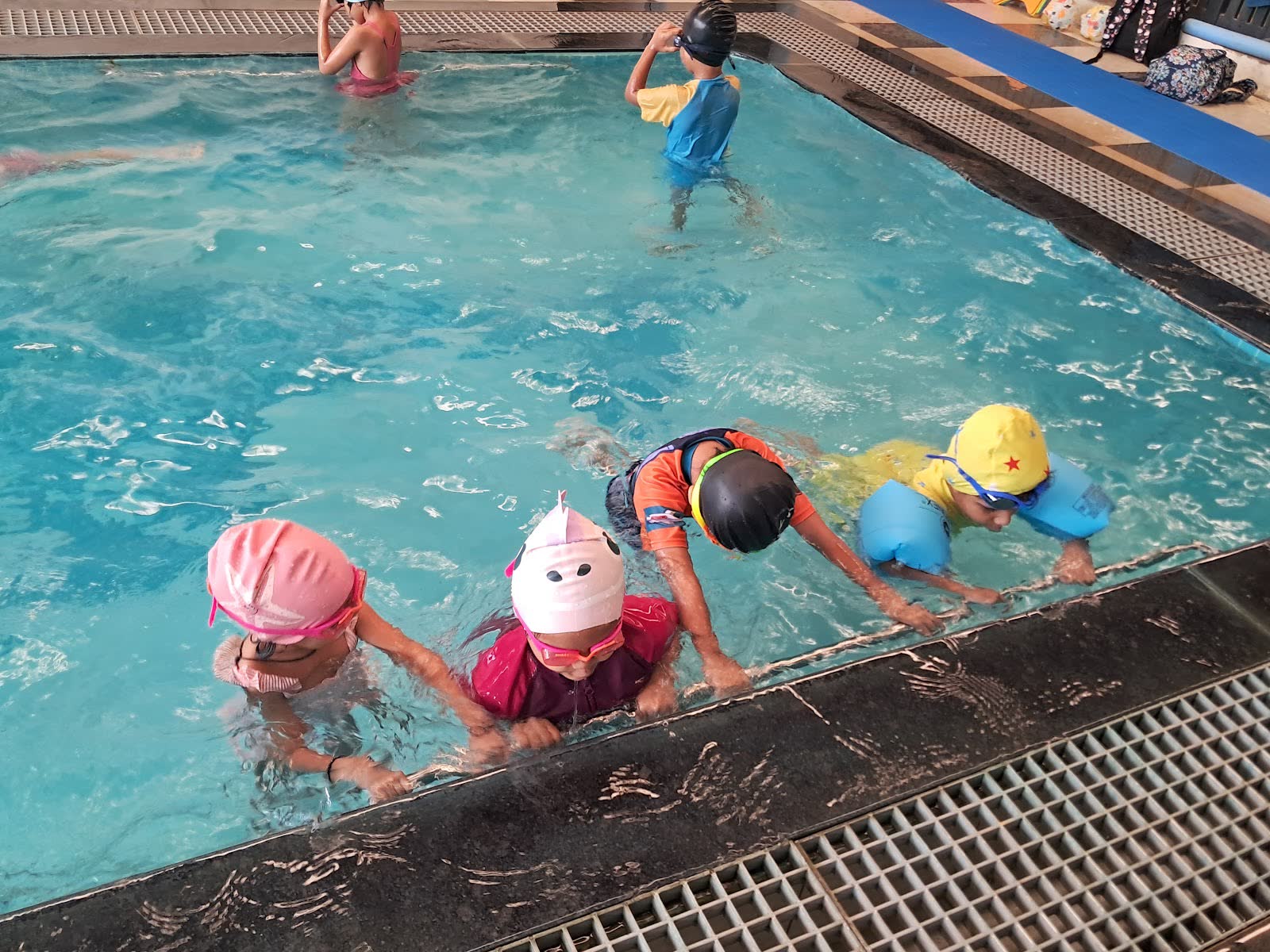 Young children in swimming caps learning to swim in the school pool
