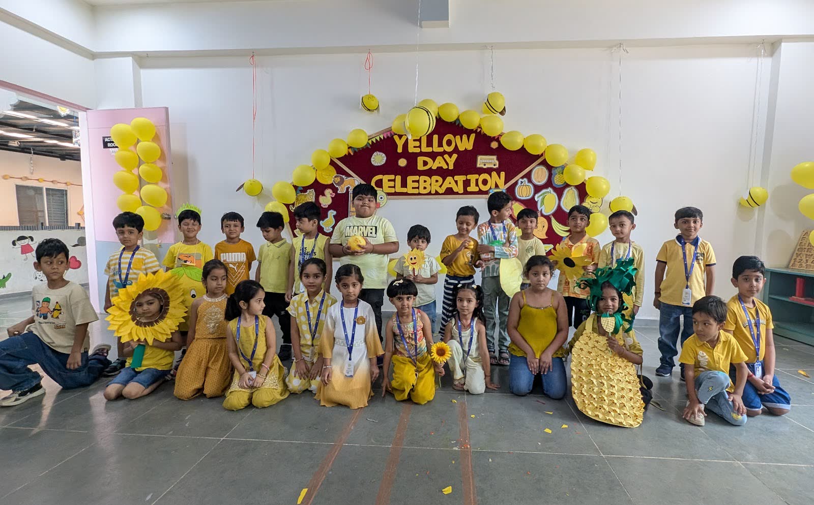 Pre-primary children dressed in yellow, seated in front of a Yellow Day celebration board