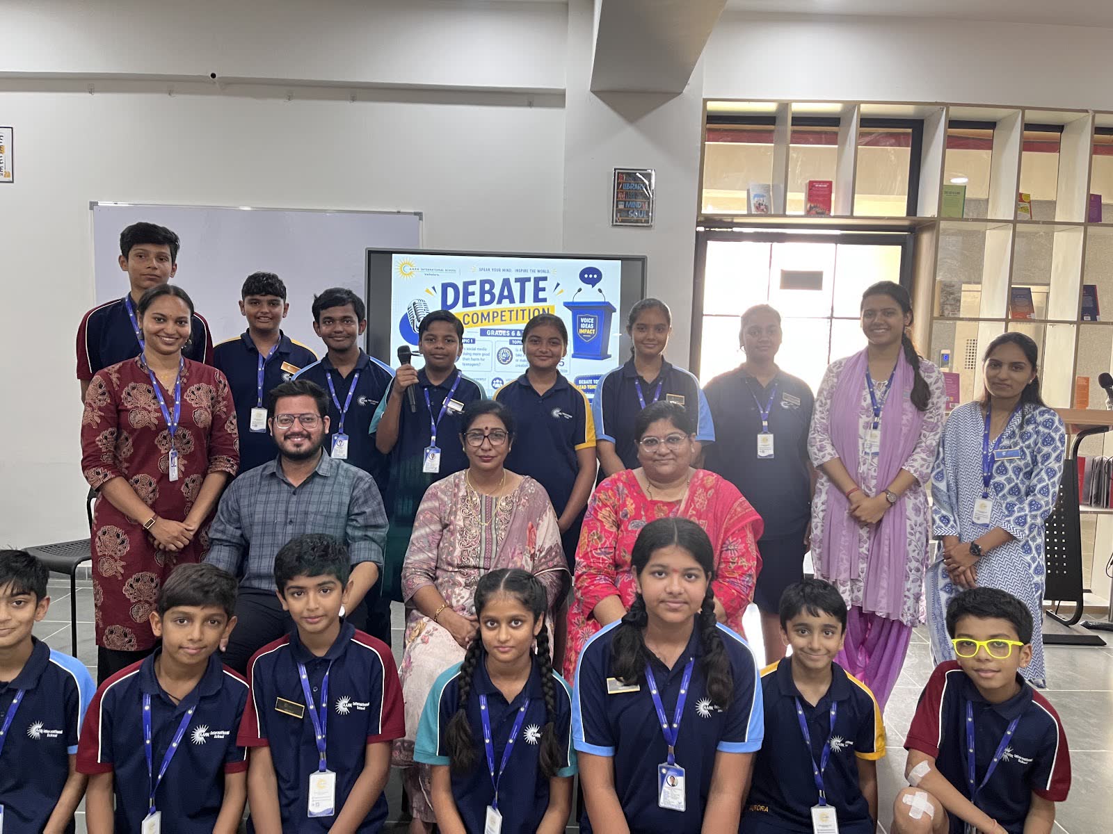 AARK debate team students with their teachers in front of a debate competition screen